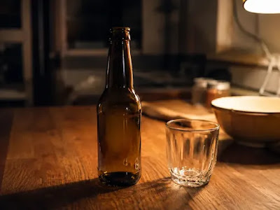 "An empty beer bottle and glass on a wooden table under warm lamp light, representing the hidden calorie cost of alcohol."