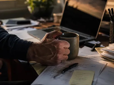 "A hand gripping a coffee mug on a cluttered office desk, representing chronic work stress and its effect on belly fat."
