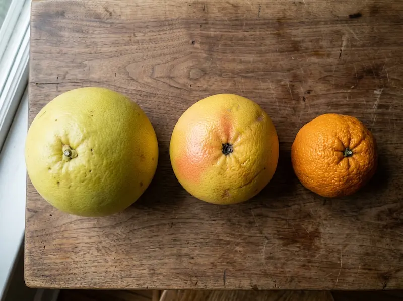 A grapefruit, pomelo, and Seville orange arranged on a wooden table, representing citrus fruits that share dangerous drug interactions.
